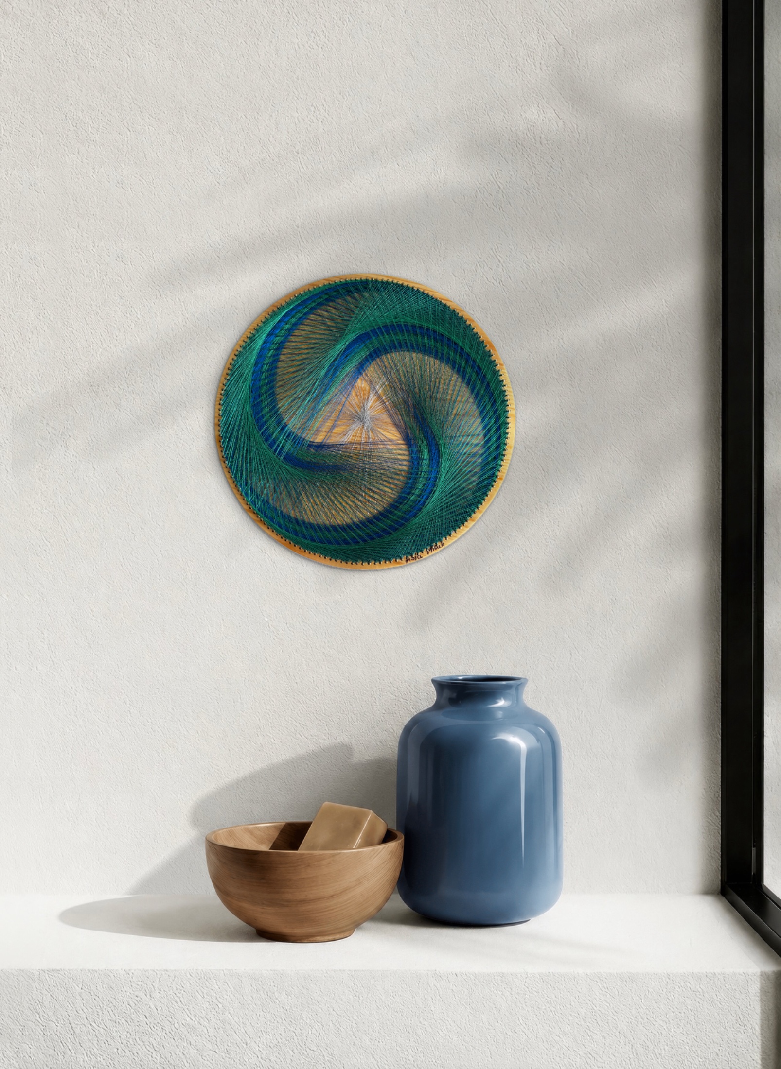 Blue green spiral string art displayed beside a blue vase and wooden bowl